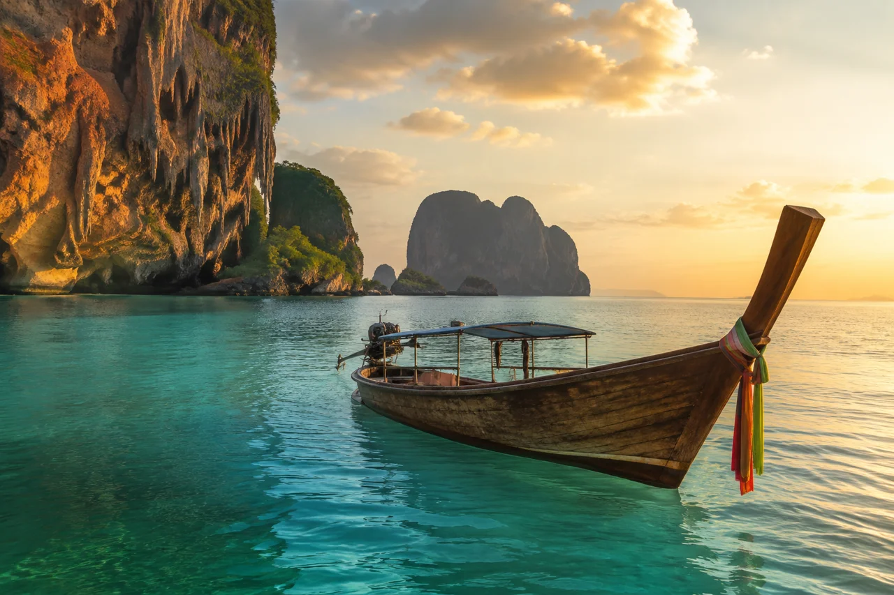 Bateau longtail sur une eau turquoise devant les falaises calcaires de Krabi en Thaïlande