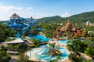 Vue panoramique d’un parc aquatique tropical à Pattaya avec toboggans, piscines, zones ombragées et palmiers.