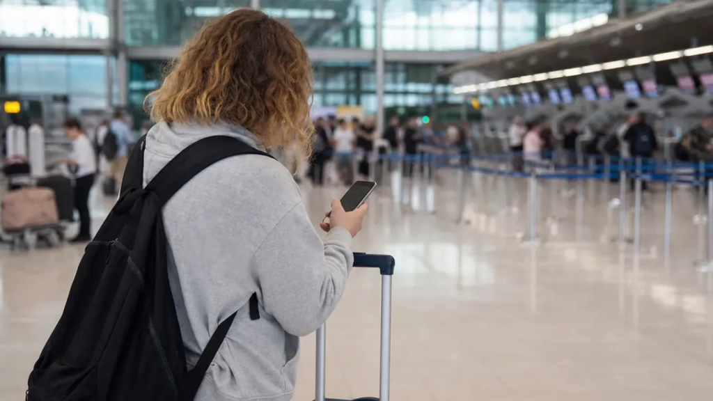 Voyageur français de dos au terminal avec valise et smartphone