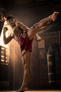 Photographie sportive dynamique d'un pratiquant de Muay Thai exécutant un coup de pied circulaire au ralenti dans un gymnase