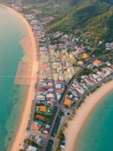 Vue aérienne d'une ville côtière tropicale avec une plage en arc, des rues quadrillées, des collines verdoyantes et des éléme